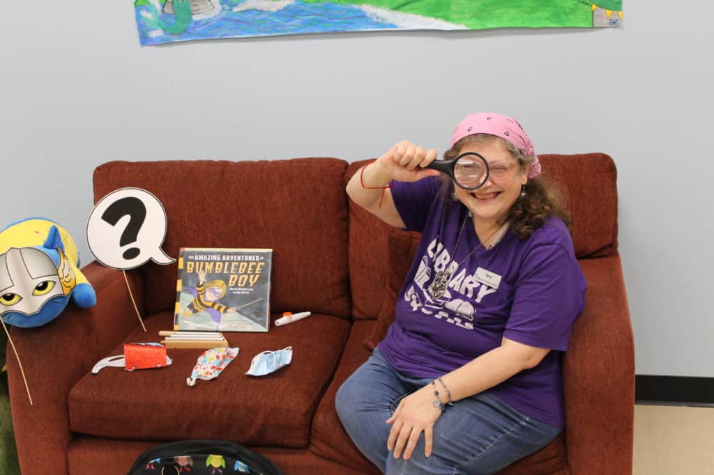Ms. Tara looking through magnifying glass with story time supplies around her.